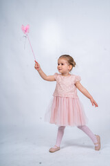 Rear view of a little girl in a pink tutu and ballet slippers, standing gracefully with a tiara on her head, holding pointe shoes.Little ballerina practicing dance moves. 