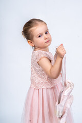 Rear view of a little girl in a pink tutu and ballet slippers, standing gracefully with a tiara on her head, holding pointe shoes.Little ballerina practicing dance moves. 