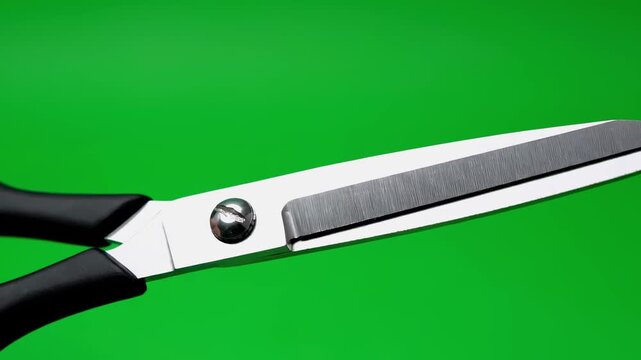 Close-up of open scissors with black handles against a vibrant green background