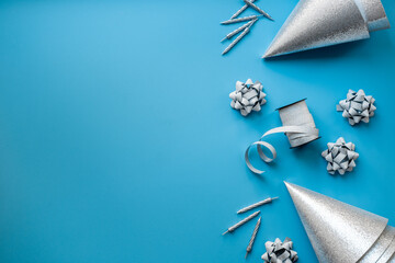 Holiday festive party flat lay with silver carnaval caps and cake candles, top view. Gift box and streamers on blue background