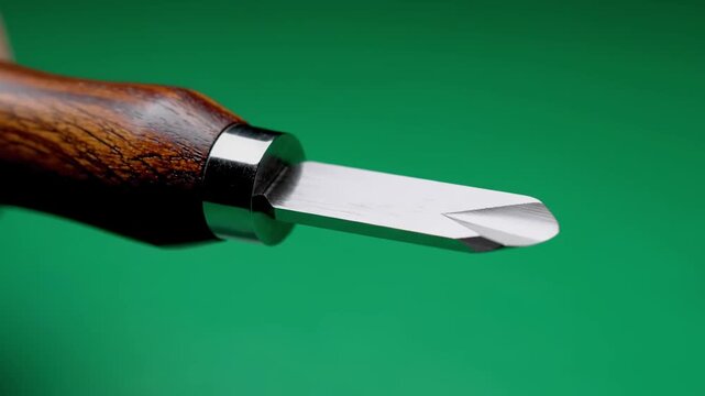 Close-up of a carving tool with a wooden handle, a shiny metallic collar and a sharp, clean blade