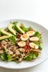 Fresh salad with avocado eggs and bacon on a white plate