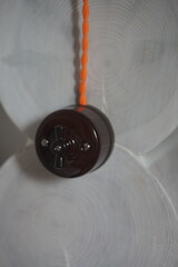 Close-up of a vintage ceramic light switch with an orange twisted cable mounted on a rustic wooden wall. Old-fashioned electrical equipment, interior detail, and retro-style decoration elements.