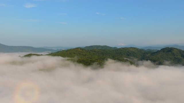 Drone footage captures the serene, fog-covered hills of Presa EL Carrizo, Tamazula de Gordiano, Jalisco. Lush greenery peeks through mist under a clear blue sky. Aerial beauty.