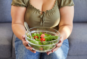Fat woman eating healthy food. Cropped shot of chubby plump overweight girl sitting on couch...