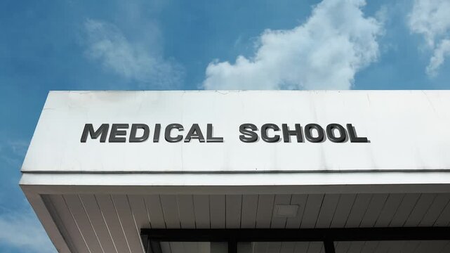 A medical school word sign prominently displayed on a large academic building under a clear blue sky, symbolizing education, future doctors, and healthcare training