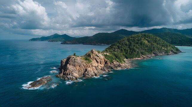 Dramatic aerial view captures rugged coastline, rocky outcrop, and dense tropical vegetation under stormy skies