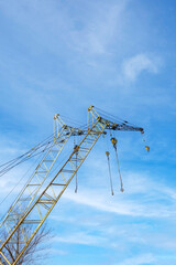 Crane is suspended in the air with a blue sky in the background. The crane is tall and has a lot of ropes attached to it