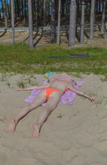 Woman is laying on a towel on the beach. She is wearing a bikini and is laying on her stomach