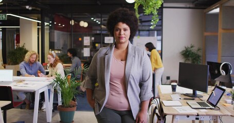 Leading Black manager wearing gray blazer guiding team in modern open-plan office, with laptops
