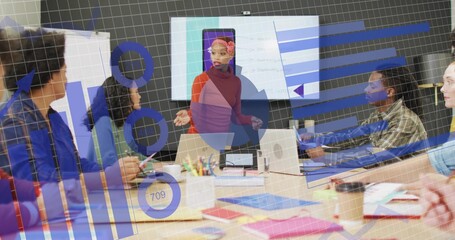 Presenting mid adult woman gesturing to data overlays in office meeting room, with laptops screen