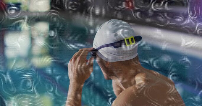 Leaning male swimmer adjusting white swim cap and goggles strap behind mesh panel at pool edge