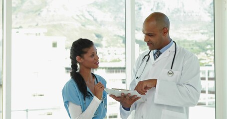 Reviewing data on tablet nurse in scrubs and doctor in coat near hospital window with stethoscope