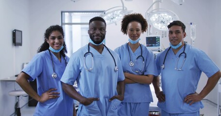 Standing surgical team wearing blue scrubs in operating theatre, with stethoscopes, surgical lights