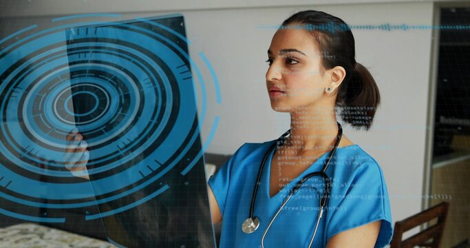 Examining doctor in blue scrubs holding panel with HUD at clinic desk with stethoscope, copy space