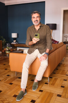 Smiling man sitting on sofa using phone in modern living room