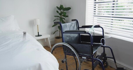 Displaying bedroom with wheelchair occupying center-right featuring bed nightstand lamp blinds