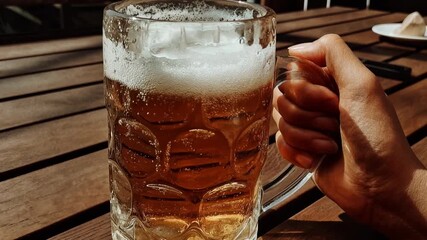 Frosty glass of beer clinking on a wooden table in golden light, creamy foam and crisp refreshment captured for bar promos, Oktoberfest themes, craft brewery ads, and relaxed weekend social content