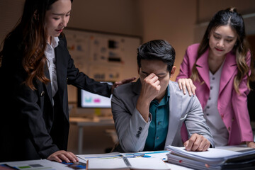 Colleagues supporting stressed businessman experiencing burnout in office