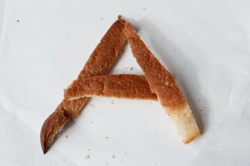 Creative letter made from burnt bread crust on white paper background. An abstract alphabet font concept for typography design food art and simple rustic eating