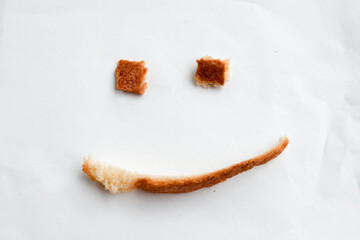 Happy smiling face made from burnt bread crust on white paper. This creative food art shows positive emotion and simple fun with delicious snack and toasty crust