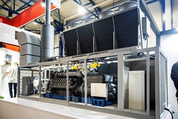 Detailed model of an industrial power generation or HVAC system, featuring a large engine, cooling units, pipes, and control elements within a metal frame, showcased at an exhibition.