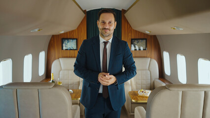 Businessman in blue suit and brown tie standing with clasped hands, confidently looking at the...