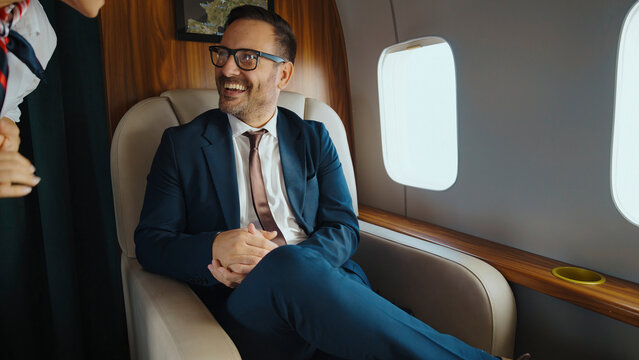 Happy businessman enjoying luxurious first class travel, interacting with a flight attendant during a private flight, representing success and executive transportation