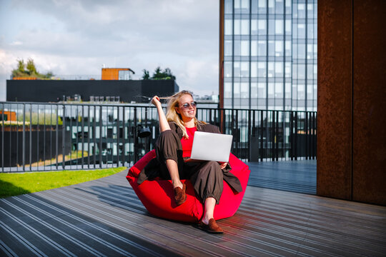 Woman working remotely outdoors on a bean bag with laptop and sunglasses