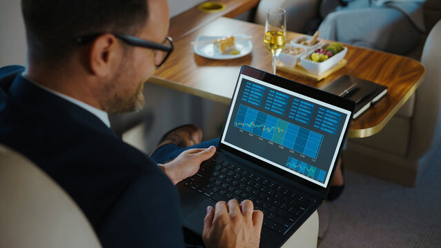 Businessman focused on financial charts and graphs on a laptop screen, managing investments and trading while traveling in a luxurious private jet cabin
