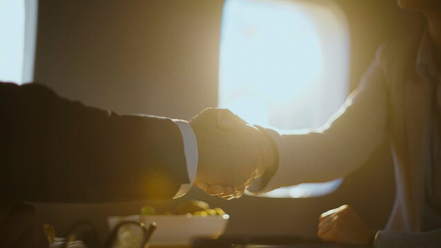 Professionals confirming a successful partnership with a handshake during a corporate flight, symbolizing agreement and collaboration in air travel with bright sun background