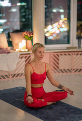 Yoga trainer in red activewear lifts her legs upward while balancing on a mat, performing an advanced pose that showcases strength and flexibility in a serene studio.
