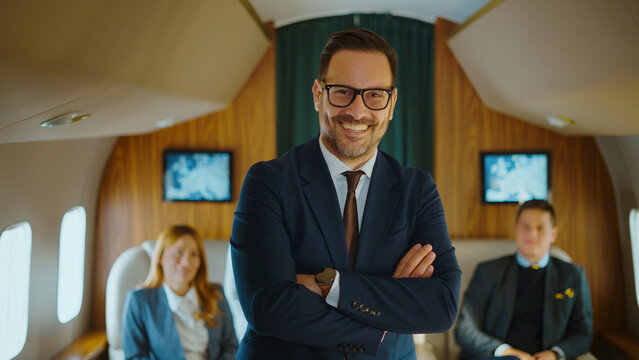 Successful businessman smiling confidently with arms crossed, flying on a private jet with his corporate team in background, symbolizing business travel, luxury, and success