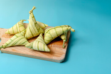 Traditional Malaysian ketupat palas neatly wrapped in palm leaves, placed on a wooden board against...