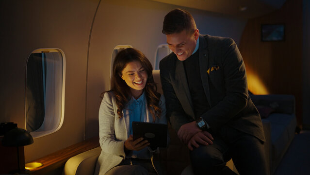 Business partners enjoying a comfortable flight on a luxurious private jet, sharing a laugh while watching content on a digital tablet during a successful trip - Powered by Adobe