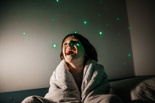 Child laughing wrapped in blanket under starry night light in bedroom