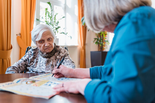 Woman taking care of old woman doing crossword puzzle