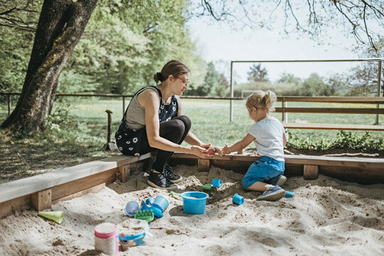 Mother playing with little daughter in sandbox on a playground