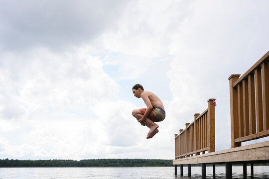 Boy in swimsuit jumping off dock into lake on a summer day