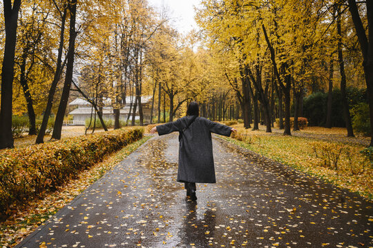Woman walking in autumn park with outstretched arms and wearing a coat