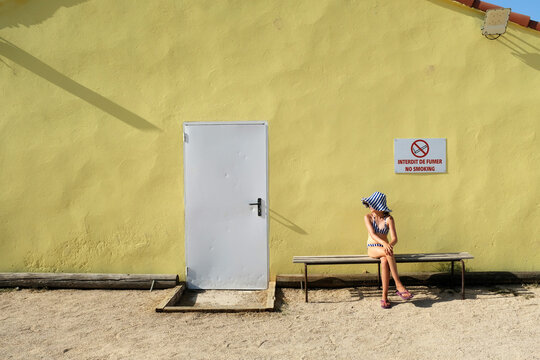 Child in striped summer hat sitting on bench by yellow wall in Marseille
