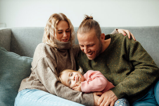 Smiling parents looking at daughter resting on lap at sofa