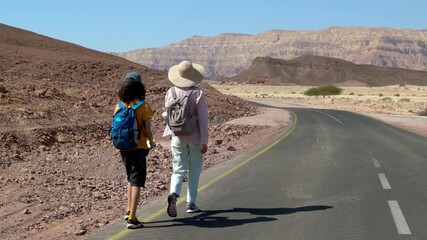 A boy with a backpack and a map walks alongside his mother along a desert trail. Family trekking. Timna National Park. The child is actively spending time. Trekking and hiking. - Powered by Adobe