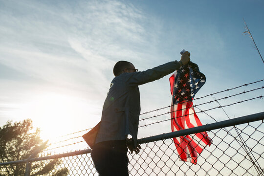 Young man removing US-American flag from brabed wire fence
