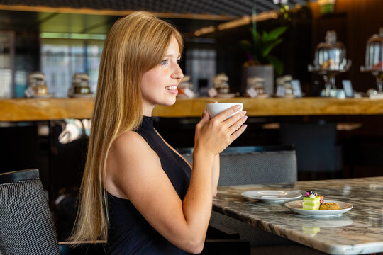 Woman enjoying coffee in modern cafe, seated at marble table, surrounded by desserts, inviting atmosphere, relaxation concept.
