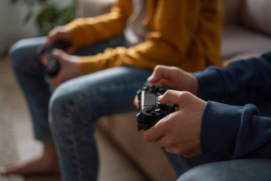 Hands of boys holding gaming consoles at home