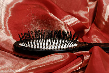 Hairbrush with hair strands on red fabric illustrating personal care