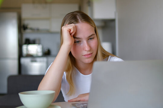 Thoughtful woman working remotely on laptop in home office