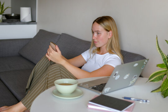 Woman sitting at home working remotely on laptop and smartphone