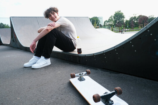Smiling boy sitting on half pipe at skateboard park